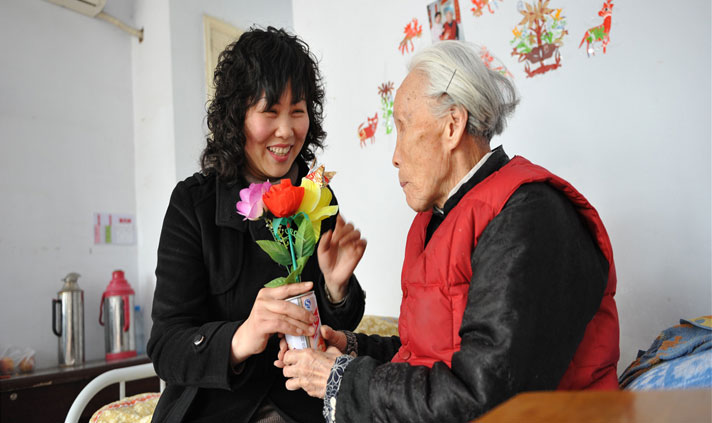 2014年11月5日，宋丽萍来到敬老院看望97岁的冀岳氏老人，老人正在把自己手工制作的鲜花交到宋丽萍的手上。.png