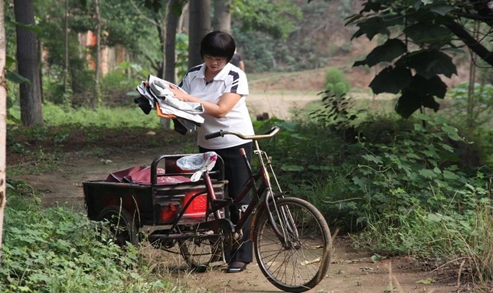 李春风骑着自己的三轮车走家串户回收旧衣服。.png